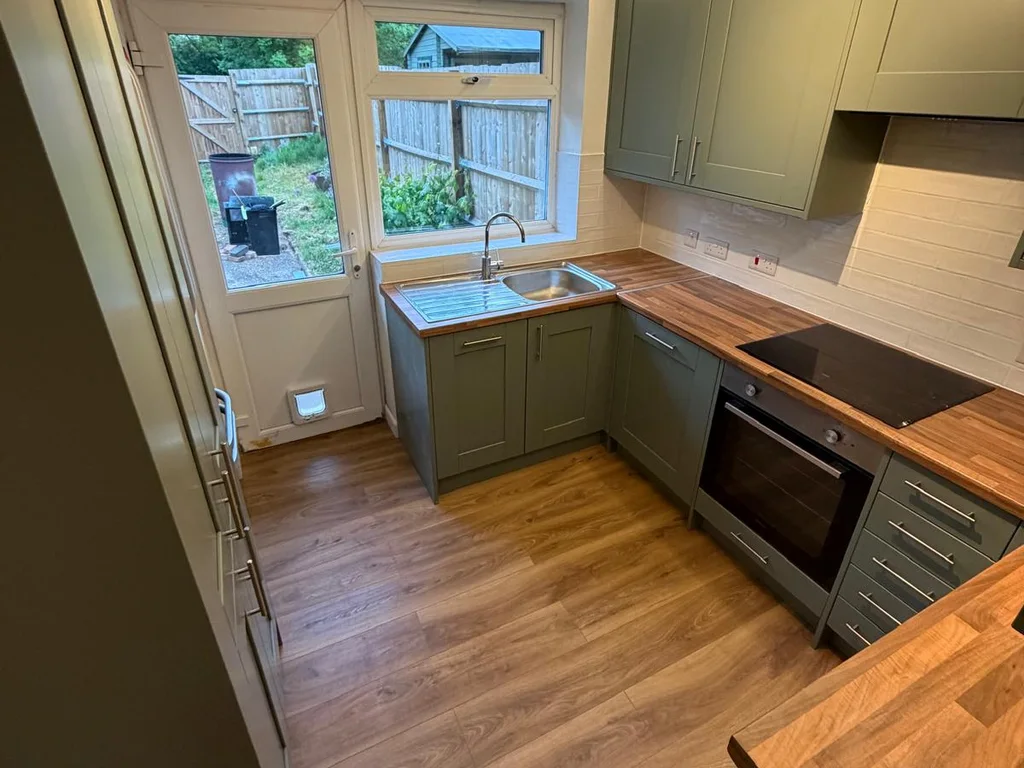 Green shaker kitchen with wood-effect worktops and a stainless steel sink